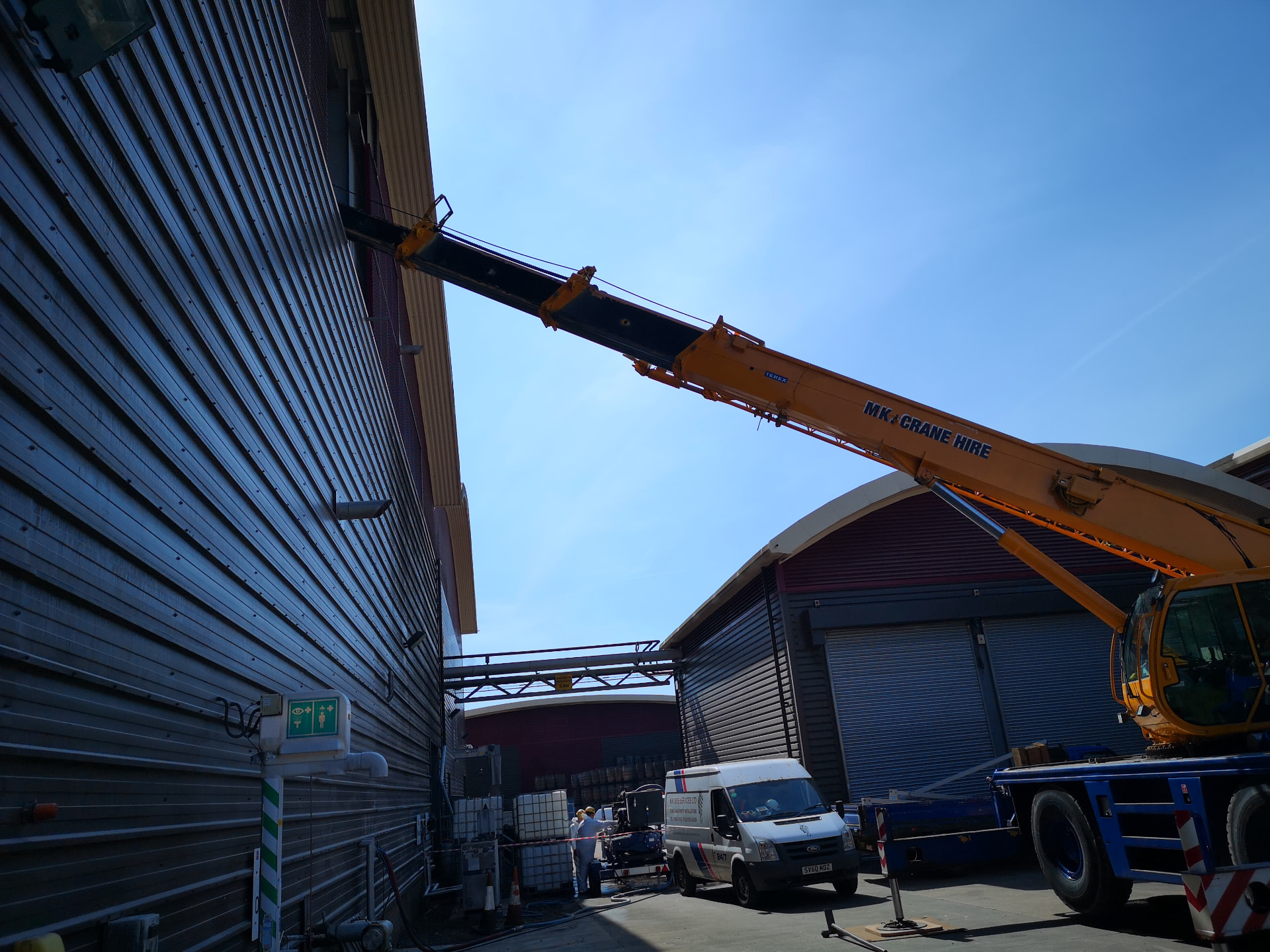 MK Site Services crane extending its jib through an industrial building opening for specialist internal lifting